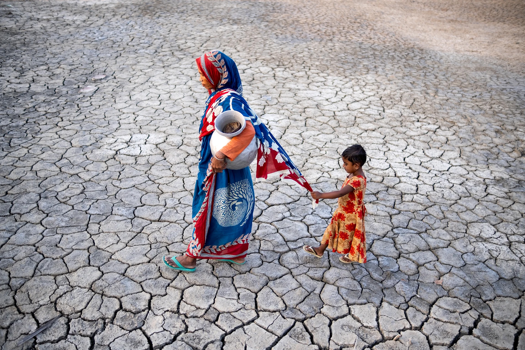 A woman and her daughter walking on extremely dry ground.