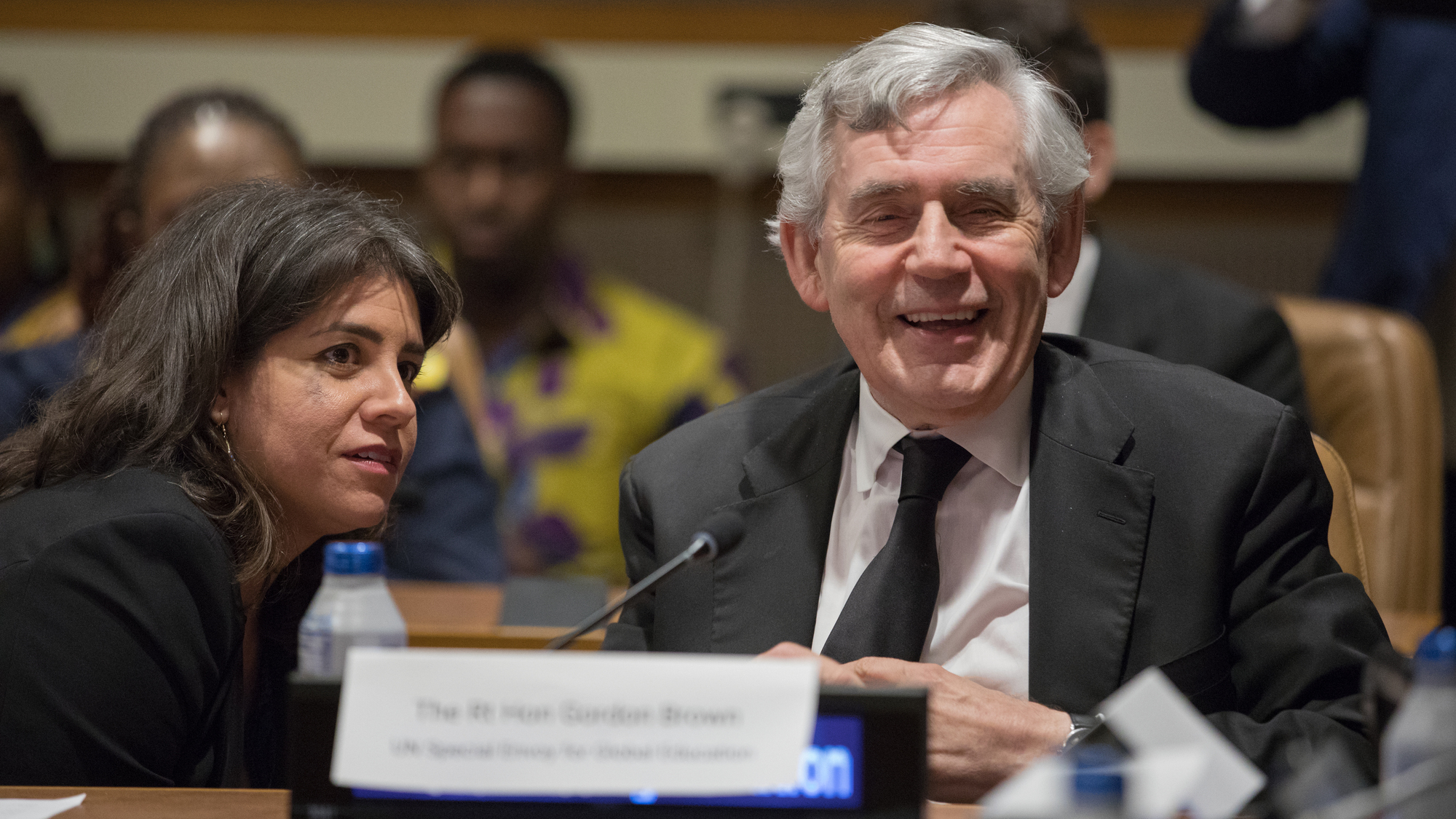 Gordon Brown is seen sitting at a table with his name plate. He is smiling in a relaxed happy mood.