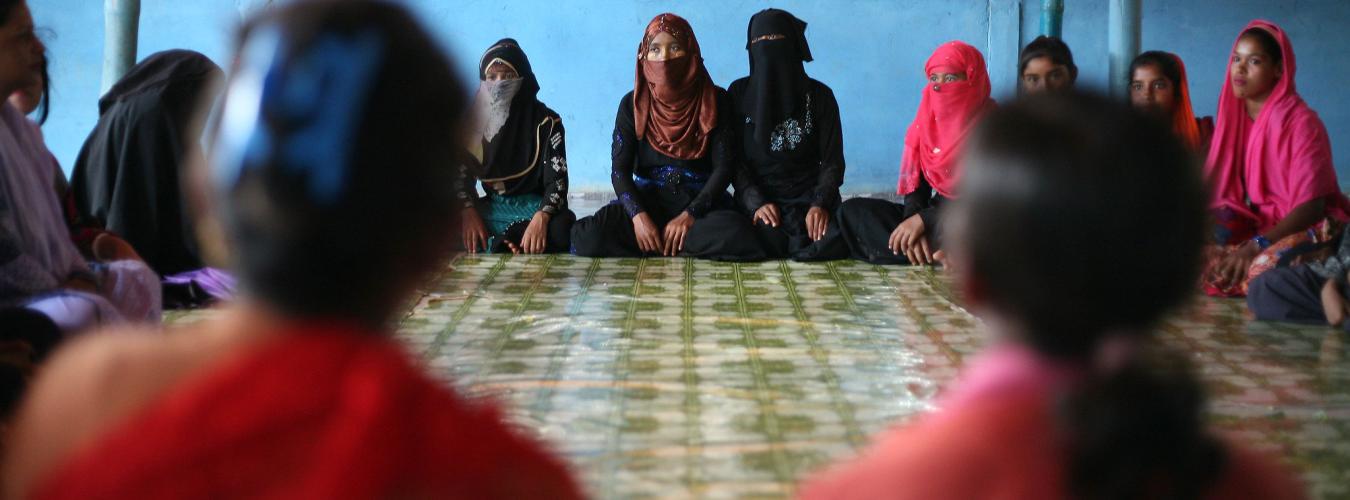 Young women are seated indoors in a large circle