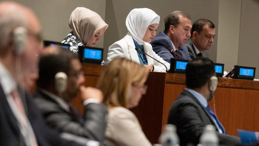 young woman with white head scarf addressing meeting from dais