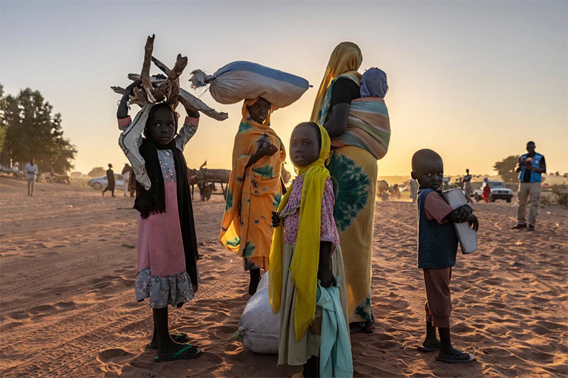 Sudanese mother and children on sand holding possessions