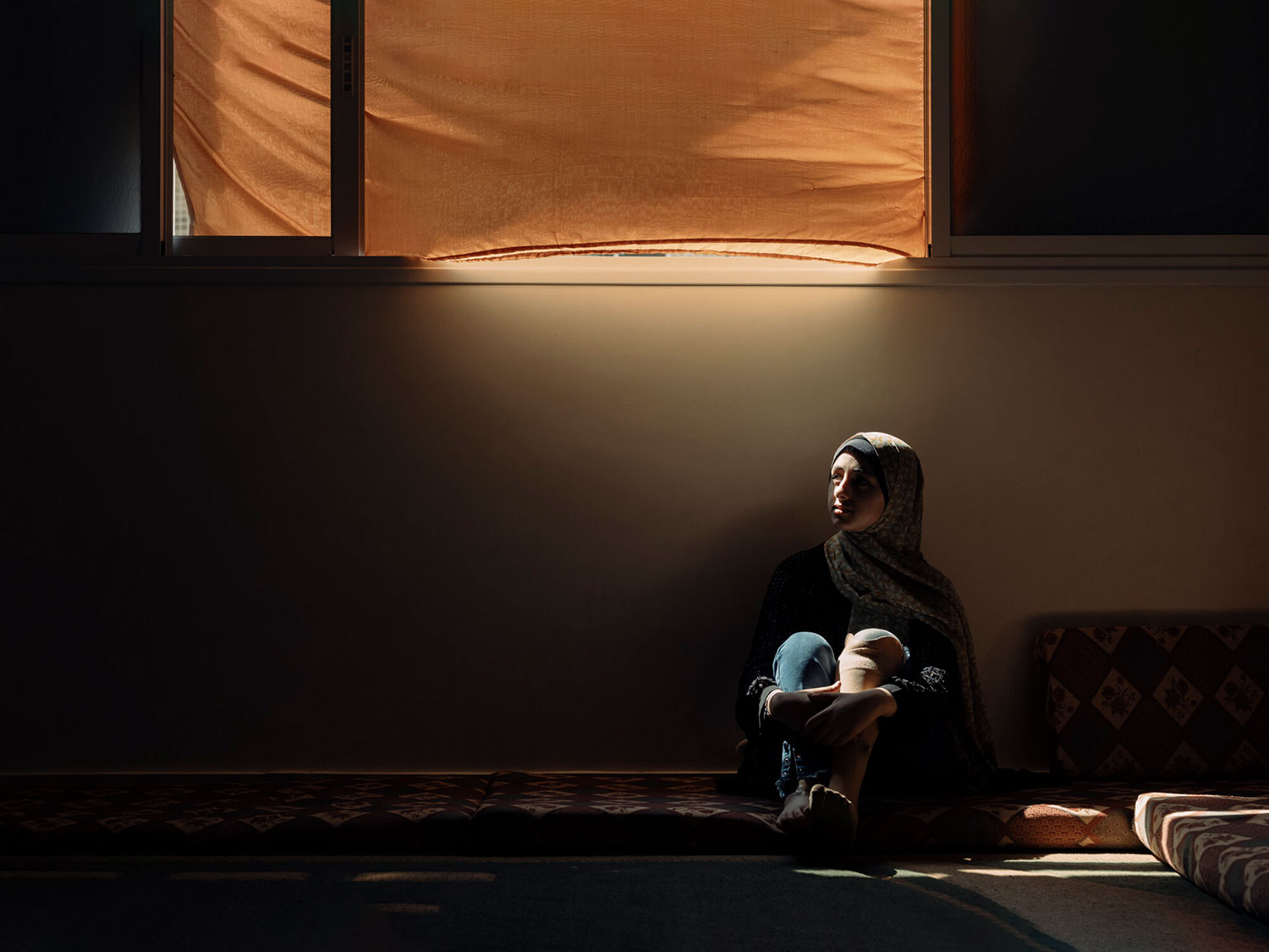 Weam sitting on the floor of a dark room with her prosthetic foot showing