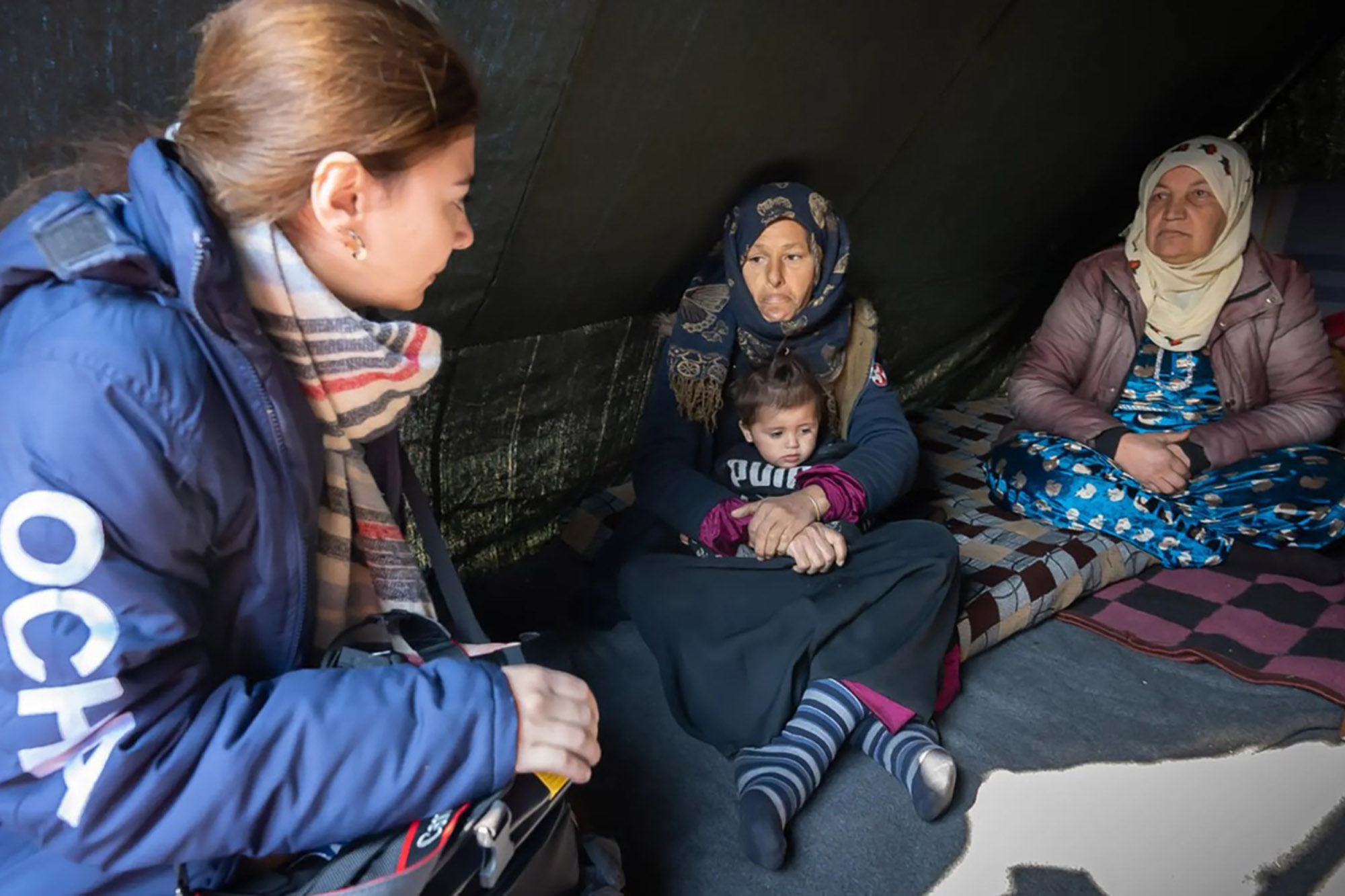 An OCHA staff member assists individuals in a temporary shelter. 