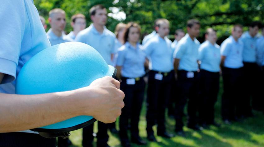 Person holding blue helmet in front of row of people in uniform