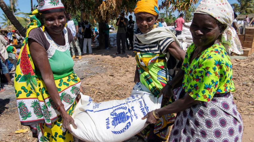 Three women carry a bag of grain