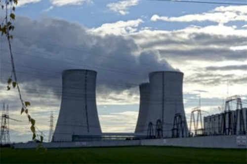 A nuclear power plant in the distance contrasts against a blue sky with clouds.