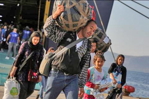 A man carrying belongings on his back walks in front of his family as they leave ship.