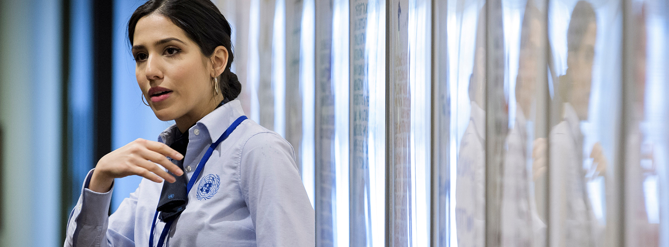 UN tour guide dressed in uniform stands inside UNHQ building and behind her is a repeat reflection of her image.