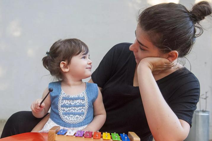 A woman and a girl, both smiling, sit together with a toy in front of them.