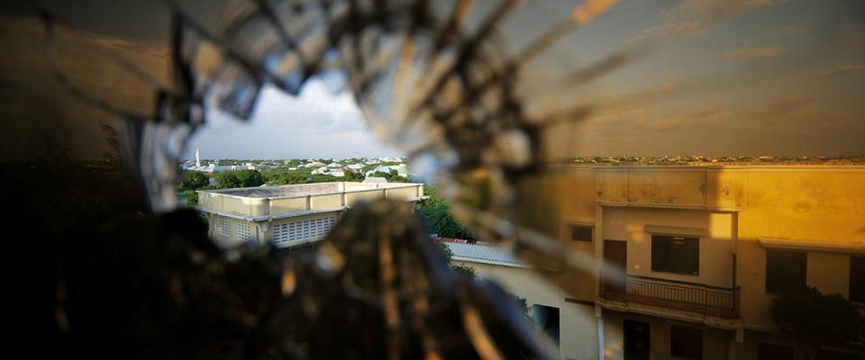 A photograph taken from the perspective of a person aiming a gun through a pane of shattered glass