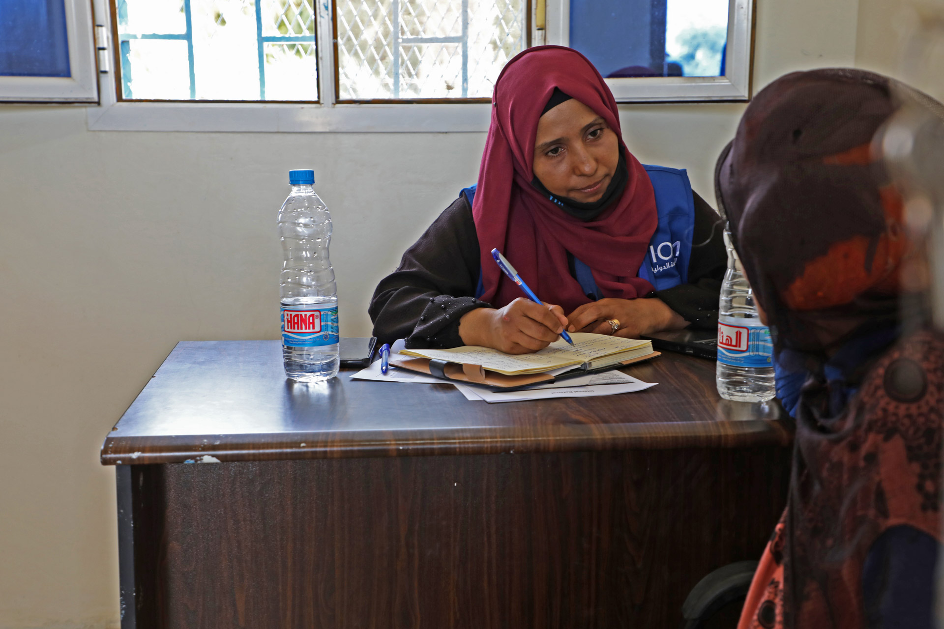 woman behind desk listening to another woman and taking notes