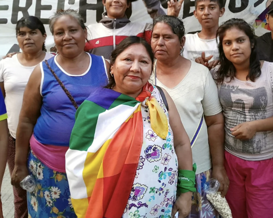 A photograph of a group of women, with the central figure draped in a colourful flag