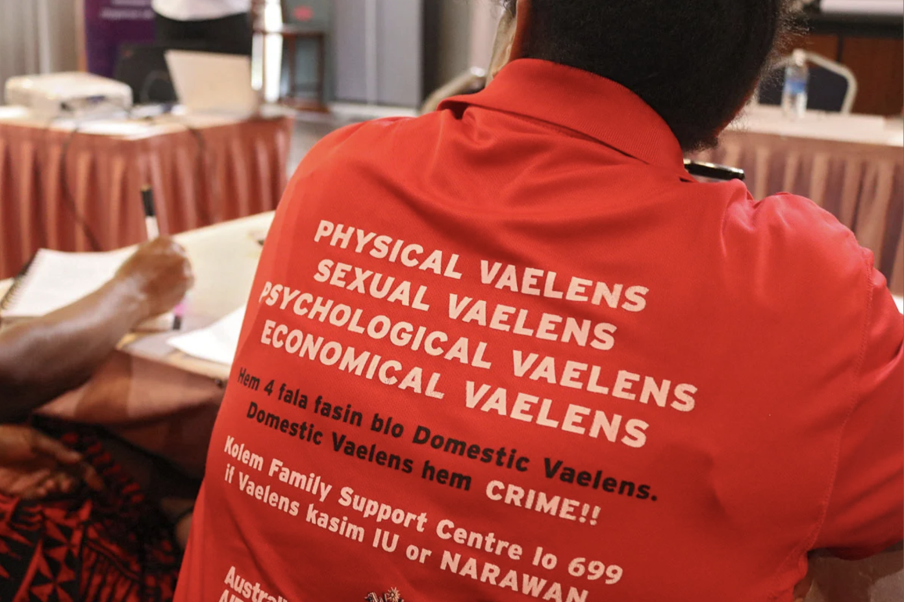 A photograph of a person showing the back of their orange sweatshirt, showing messages against violence against women